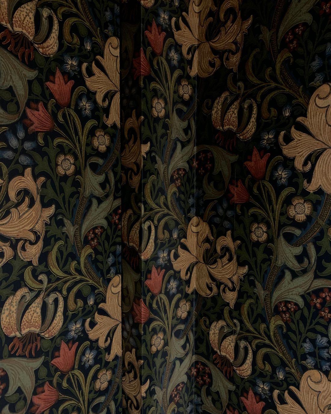 Close-up of a dark arts-and-crafts style wallpaper with ochre lilies, red tulips and twisting green foliage