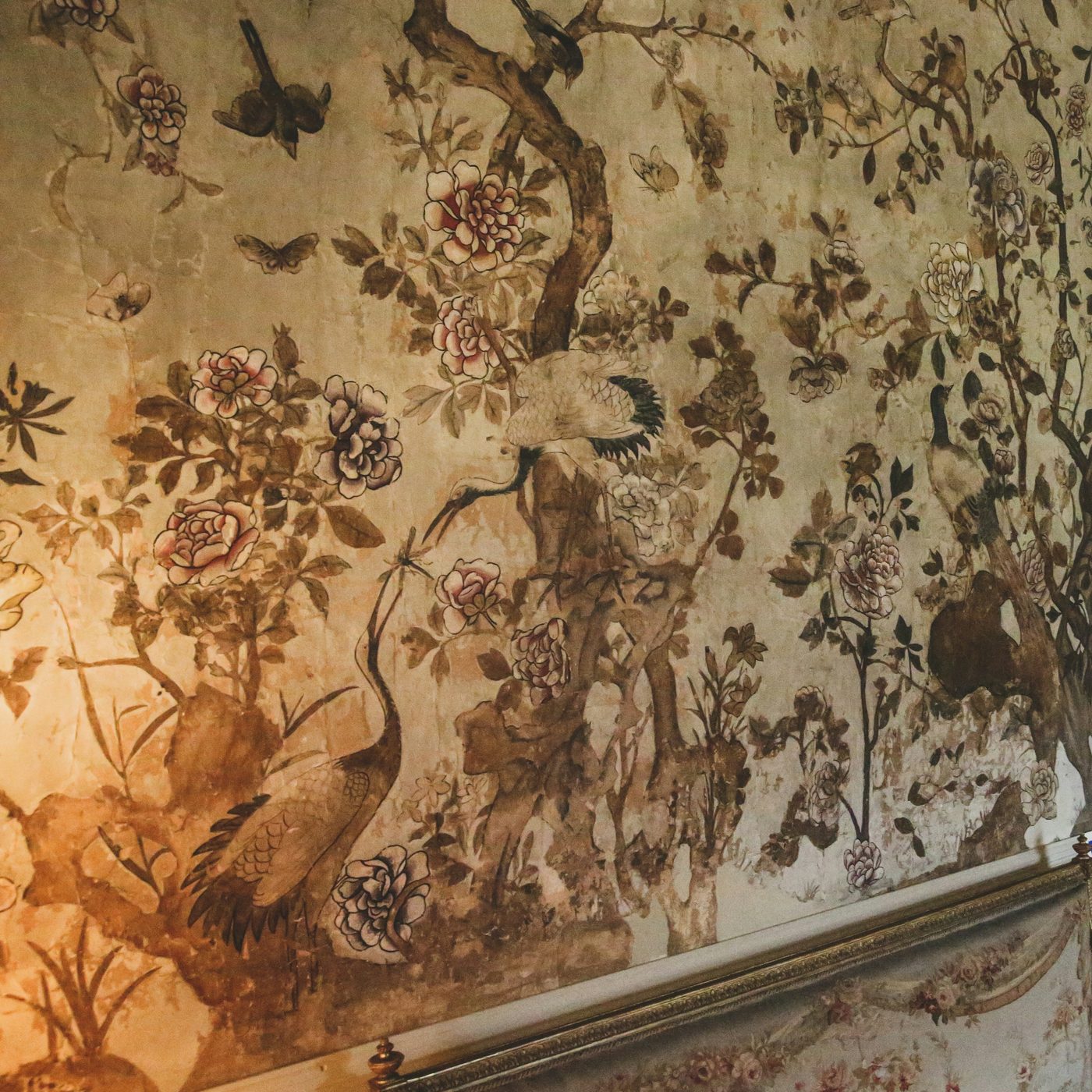 Hand-painted chinoiserie wallcovering with cranes, peonies, birds and flowering branches above a gilded settee rail