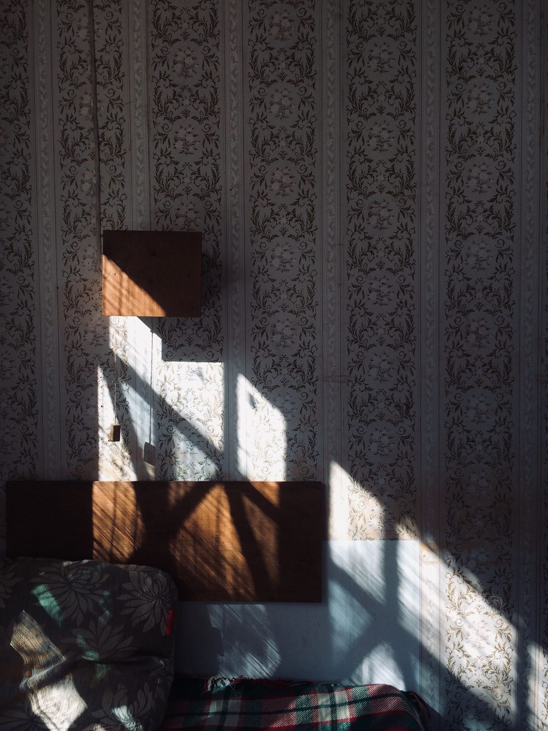 Grey ornamental stripe wallpaper crossed by window light and shadow above an upholstered chair