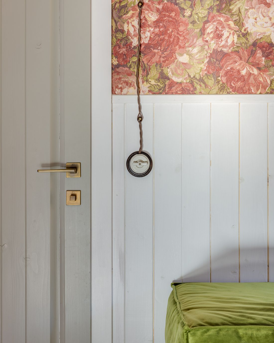 Large-scale rose floral wallpaper above white tongue-and-groove wainscoting, beside a door with brass handle