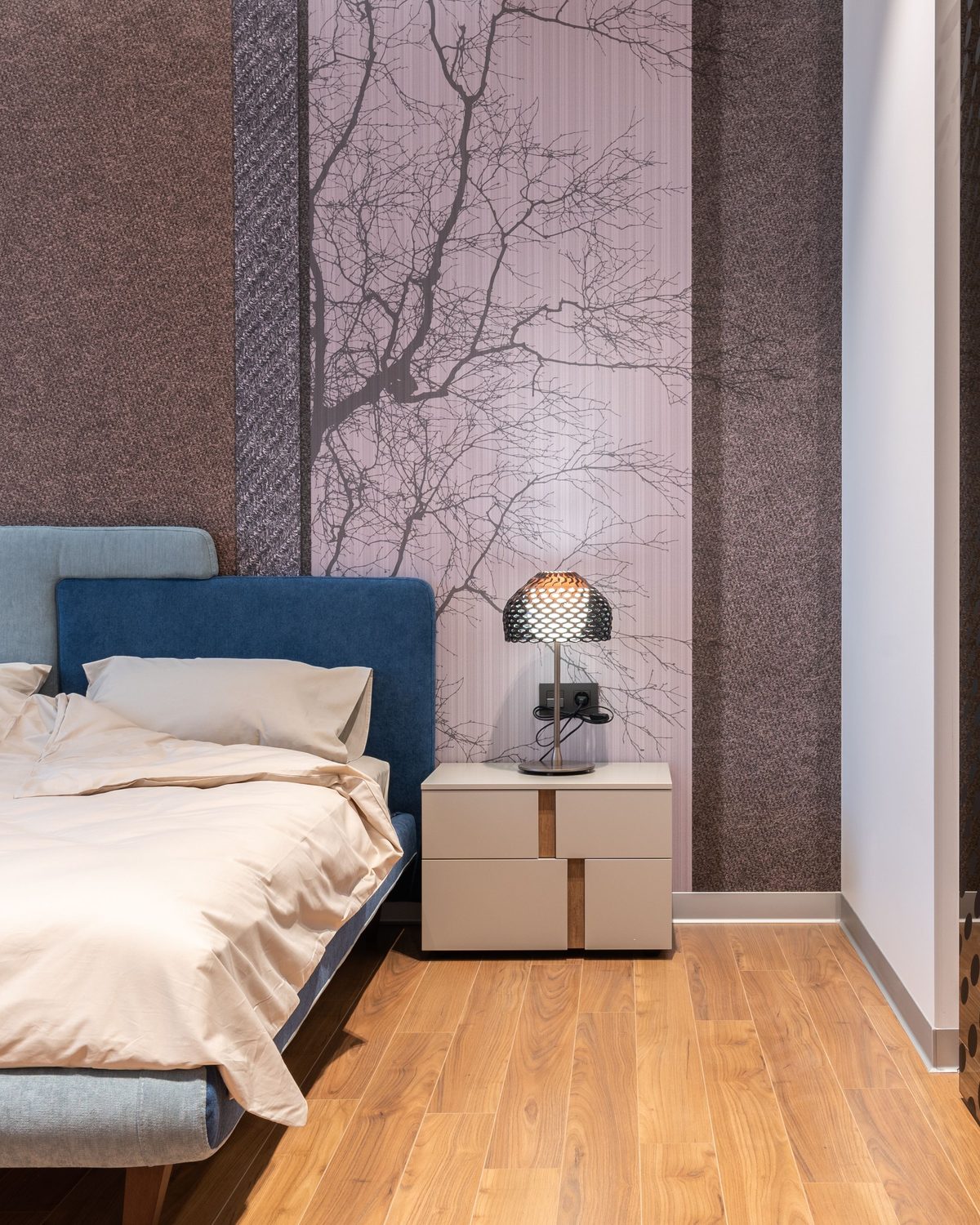 Contemporary bedroom with a soft lilac tree-branch mural panel between textured mocha wallcovering, a blue upholstered bed and a sculptural lamp